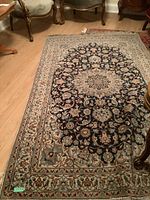 Full view of rectangular wool area rug with floral medallion and ornate border pattern. Dark navy central medallion with cream, blue, and other accent colors.