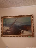 Framed landscape art piece hanging on a beige wall, featuring barren trees and snow with a signed corner.