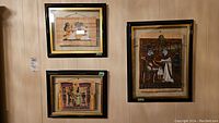 Three framed art pieces on fabric hung on a wall, showing different Egyptian scene compositions and frame styles.