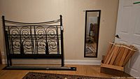 Black metal bed frame parts, wood slats in box, and a full-length wall mirror leaning against wall