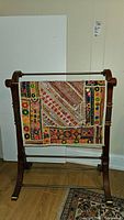 Blanket rack with colorful decorative rug draped over front metal bar, showing patterned embroidery