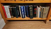 Shelf of mixed hardcover and paperback books including works by Tom Clancy, Ernest Hemingway, and classic Russian authors.