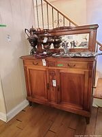 Front-left angle view of wood cabinet with framed mirror on top, showing two doors, two drawers, attached mirror, and surface scratches.
