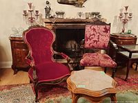 Pair of two vintage wooden framed upholstered chairs, one with deep red velvet button tufting, the other with pink floral fabric upholstery, both showing scratches and wear.