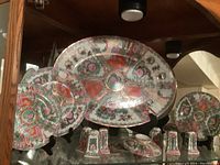 Display of china set showing large platter, two small plates and six shakers, and two bowls on shelf with stands