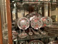 Shelf display of 11 decorative plates, 6 small spoons, and plate stands showing intricate colorful Chinese patterns with floral and figure scenes.