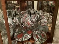 Full view of china set displayed on shelves showing plates, cups, saucers, teapot, and large bowl with floral pattern and intricate design.