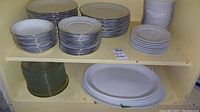 Shelving with stacks of white side plates, dinner plates, bowls, and translucent green glass plates. White oval platters on bottom shelf.