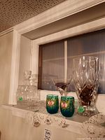 Image showing crystal decanter with stopper, tall crystal vase, two turquoise hand painted glasses with floral decorations, clear martini glass, and clear ashtrays on lace cloth.
