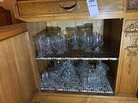 Two shelves full of clear glass mugs and dessert cups placed inside a wooden cabinet.