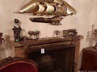 View of the fireplace mantle with silver plated wine glasses, silver plate mug, metal swans, and decorative metal mixing bowl.