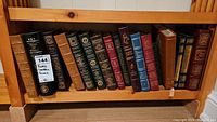 Wooden shelf holding a row of approximately 18 leather-bound books of various colors