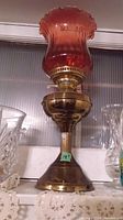Full view of the brass oil lamp with amber fluted glass shade on top, showing the shape and color details.