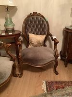 Frontal view of carved wood framed parlour chair with button-tufted velvet back and matching seat cushion with a decorative throw pillow.