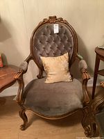 Full front view of carved wood framed chair with tufted grey velvet upholstery and a decorative pillow on the seat.