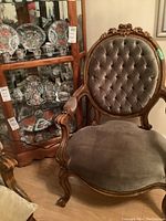 Full view of the carved wood parlour chair with tufted velvet upholstery, showing backrest and seat and part of the armrests.