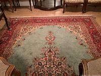 Full view of the wool hand-knotted area rug showing the central light blue field with floral medallion design and red patterned border on hardwood floor.