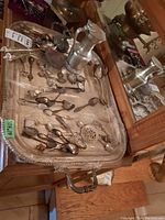 Photo showing large silver plate serving tray with assorted silver plate and pewter spoons, pewter jug, and candle holder on wooden surface.