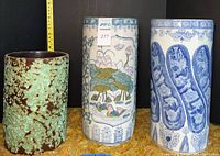 Three tall planters including two porcelain and one pottery. Porcelain planters are decorated with blue and multi-color designs, pottery planter has textured glaze.