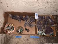 Wide view of all items in cardboard boxes showing amethyst clusters, stone eggs, and smaller rocks