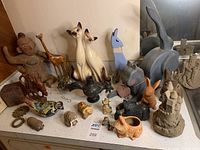 Full lot showing animal-themed home decor including the large Siamese cats, carved wooden giraffe, pottery animals, metal ladybug, sandcastles, and human figurine