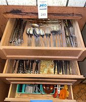 Top drawer with mixed stainless steel cutlery including forks, knives, and spoons organized side by side inside a wooden drawer