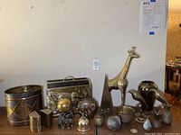 Wide shot of the brass home decor lot showing most items together on a table including giraffe, magazine holder, bookends, and small figurines.