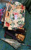Top view of floral carpet bag with wooden handles on carpet, showing stacked bags and umbrellas beneath.