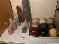 Full set of carved obelisks on left and box, cone and stone orbs on right arranged on a white surface.