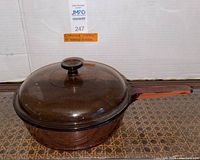 Amber glass skillet frying pan with lid on top, showing side profile with handle and lid knob