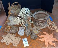 Full lot overview showing the assortment of earth-toned ceramic and terracotta planters, figurines, macramé holders, and decorative wall hangings on a tiled floor.