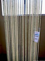 Beaded curtain hung showing 30 strands of round translucent beads in gold, peach, and light green shades hanging from a brass track.