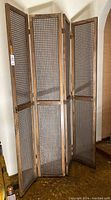 Front view of four-panel rattan room divider standing upright with natural wood frame and woven cane sections.