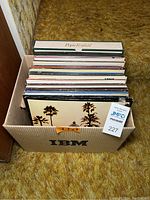 Box filled with over 50 vinyl record albums stacked upright showing a variety of album spine titles with a 'Pops Festival' boxed set album on top.
