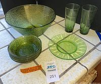 Overview of all items including large green salad bowl, four small matching bowls, two tall drinking glasses, and one green salad plate on a tiled surface.