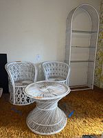 Full view of two white wicker barrel chairs, round table, and tall bookshelf with curved top and glass shelves in a room with carpet