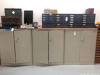 Three beige metal cabinets side-by-side, doors partially open, showing adjustable shelves inside.