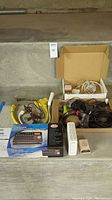 Lot showing the Tascam DP-008 box, assortment of wires and cables in a box, Motorola modem, and some connectors arranged on concrete steps.