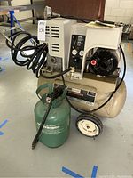 Full view of beige Sears Craftsman air compressor with attached black cords and Campbell Hausfeld green portable air tank in front.