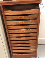 Front view of wood cabinet showing shallow drawers with orange labels for organization.