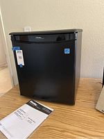 Front view of Danby compact mini fridge black exterior with instruction manual on wood surface.