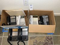 Six Panasonic desk phones inside two boxes: four black and two white desk phones with handsets and keypads.