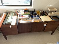 Wide shot of all drafting and desk supplies arranged on a wooden cabinet including rulers, trays, drawing tools, and supplies.