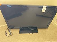 Front view of the LG 42-inch LCD TV showing the screen, stand, remote control, and power cord.