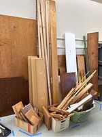 Wide view showing large plywood sheets, particleboard shelves, fence pickets, and assorted wood pieces neatly arranged against the wall and in containers.