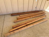 Wide view showing set of lumber posts and boards laid on concrete beside wall.
