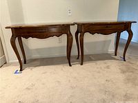 Two medium brown Ethan Allen small console tables side by side against a wall, showing front and side views. Each table has a single drawer and curved legs.