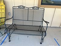 Front view of black iron swinging patio loveseat showing mesh seat and decorative backrest