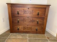 Front view of the dresser showing three carved drawers with locking keyholes and brass knobs with black wood drop handles. Visible Arabic or Middle Eastern geometric wood carvings.