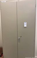 Closed beige steel double door cabinet with locking handle.